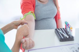 Nurse drawing blood from woman's arm with lab tubes on a table