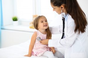 Female doctor listening to little girl's chest with stethoscope