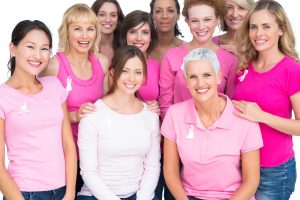 Women of all ages and ethnic backgrounds wearing pink shirts with pink cancer awareness ribbons.